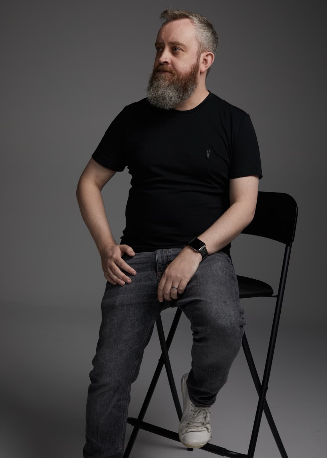 Mark Darling seated on a folding chair, black and white studio portrait